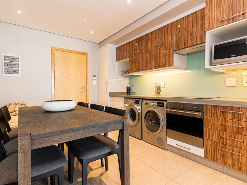 Modern open-plan kitchen featuring wood-grain cabinetry, integrated appliances, glass splashback, and tiled flooring, seamlessly flowing into the dining area.