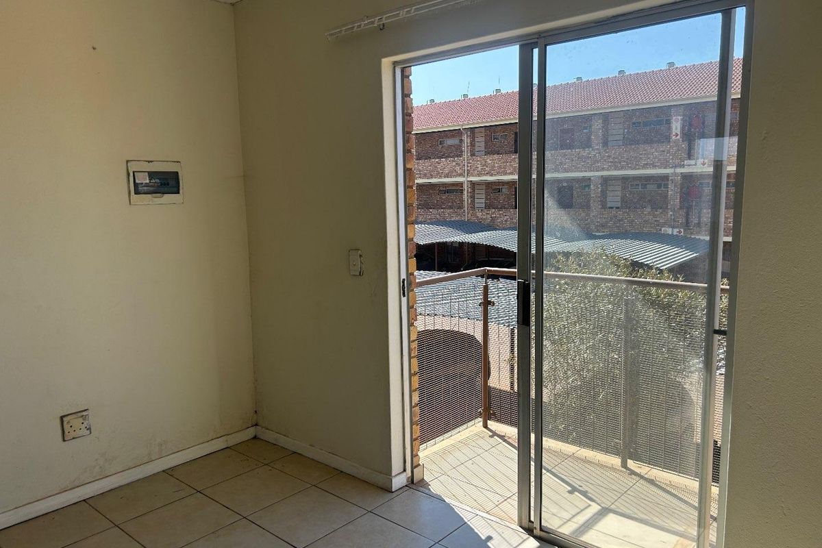An empty bedroom featuring tiled flooring and a sliding glass door that opens onto a small balcony with views of the complex.