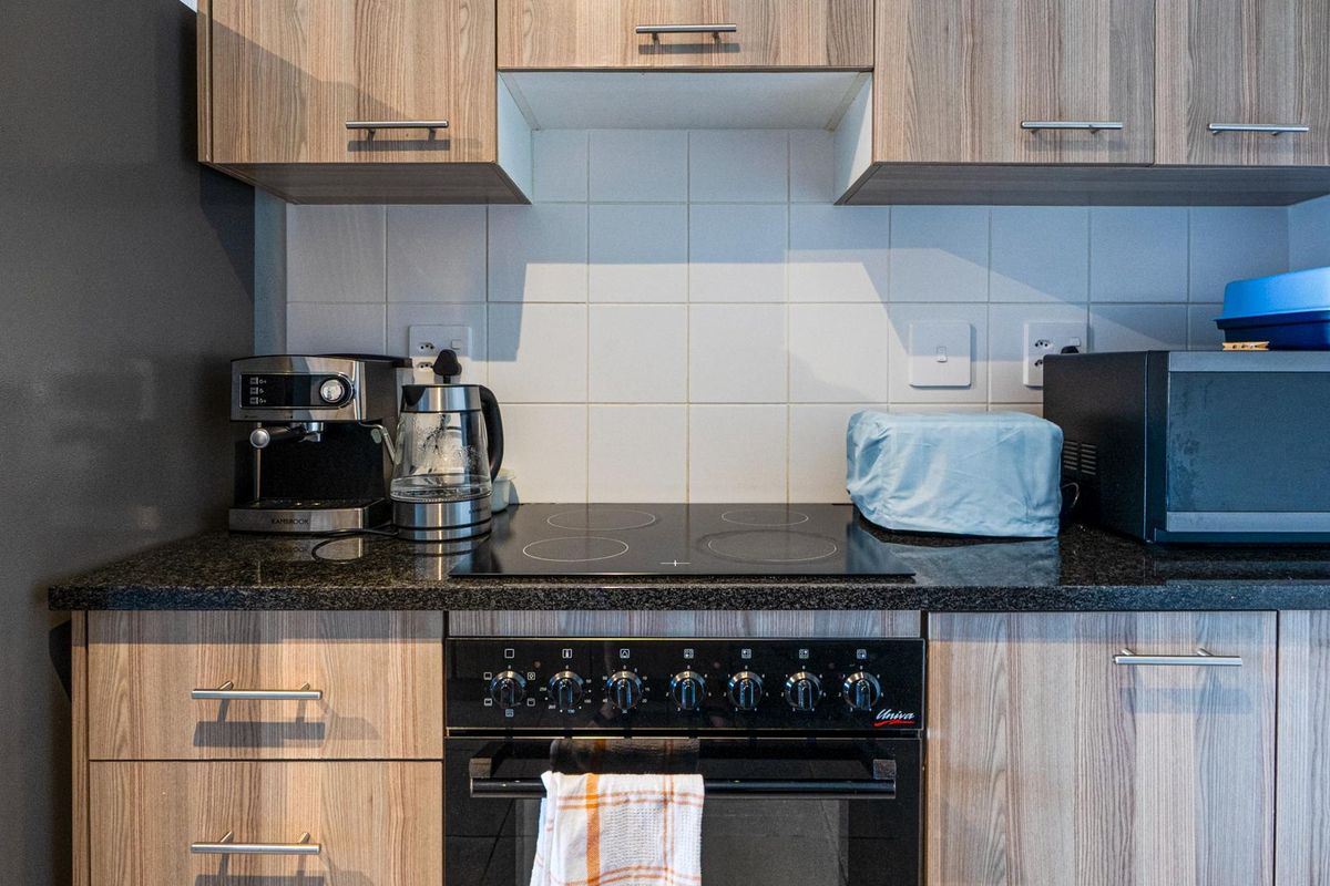 A functional kitchen area featuring wood-grain cabinetry, a dark granite countertop, and a built-in electric oven with a ceramic hob.
