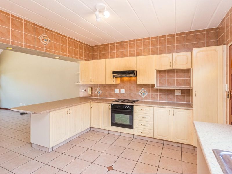 A spacious, functional kitchen featuring light wood cabinetry, tiled backsplash, built-in oven and hob, and a convenient breakfast bar overlooking the living area.