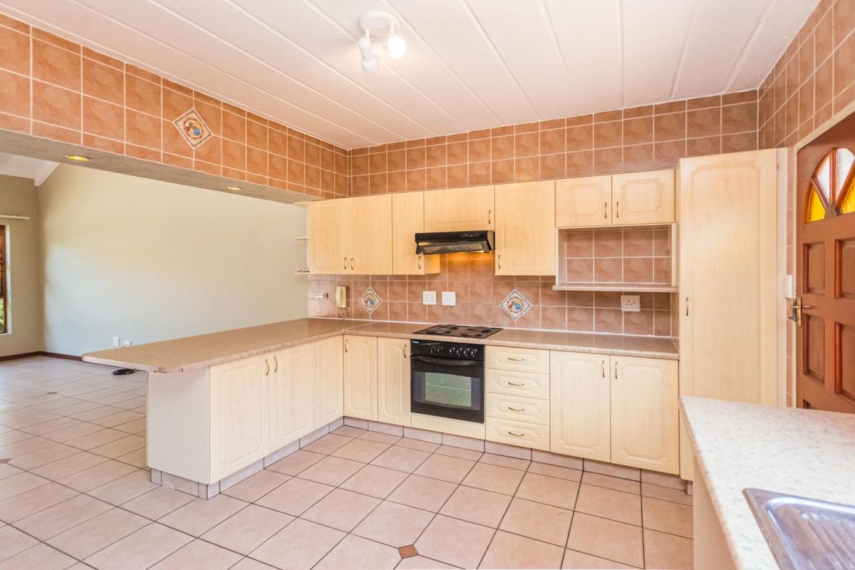 A spacious, functional kitchen featuring light wood cabinetry, tiled backsplash, built-in oven and hob, and a convenient breakfast bar overlooking the living area.