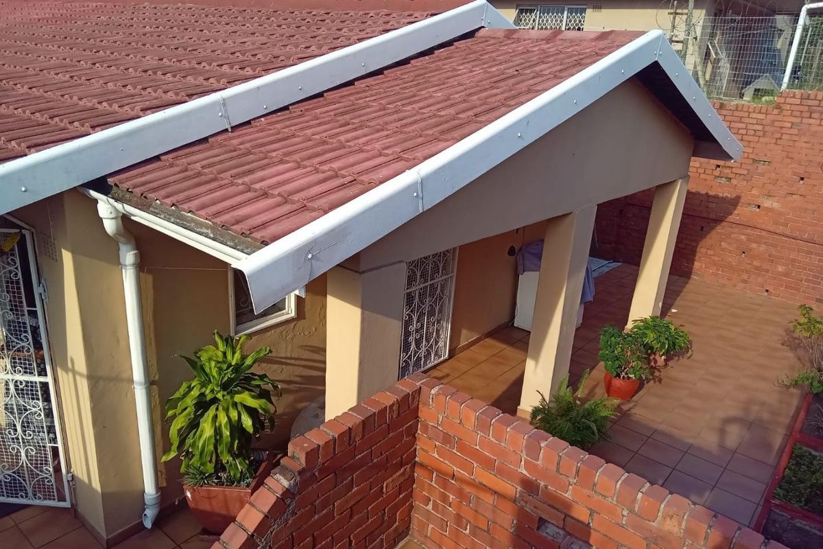 A rear view of the property featuring a covered patio area, tiled roofing, and brick boundary walling.