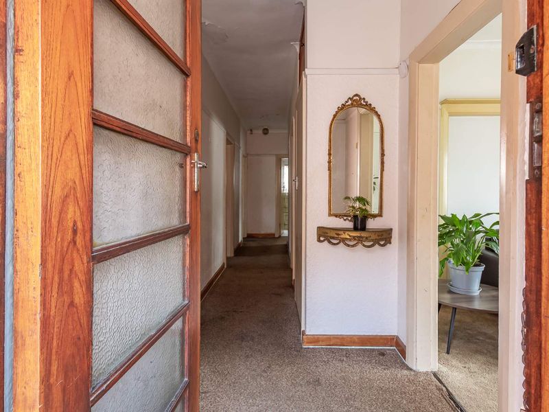 A functional hallway featuring timber door frames and textured glass, providing access to adjacent rooms. The space requires cosmetic updates to finishes.