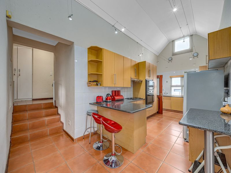 Spacious kitchen featuring light wood cabinetry, granite countertops, built-in oven, and vaulted ceilings with track lighting, leading to a raised hallway area.