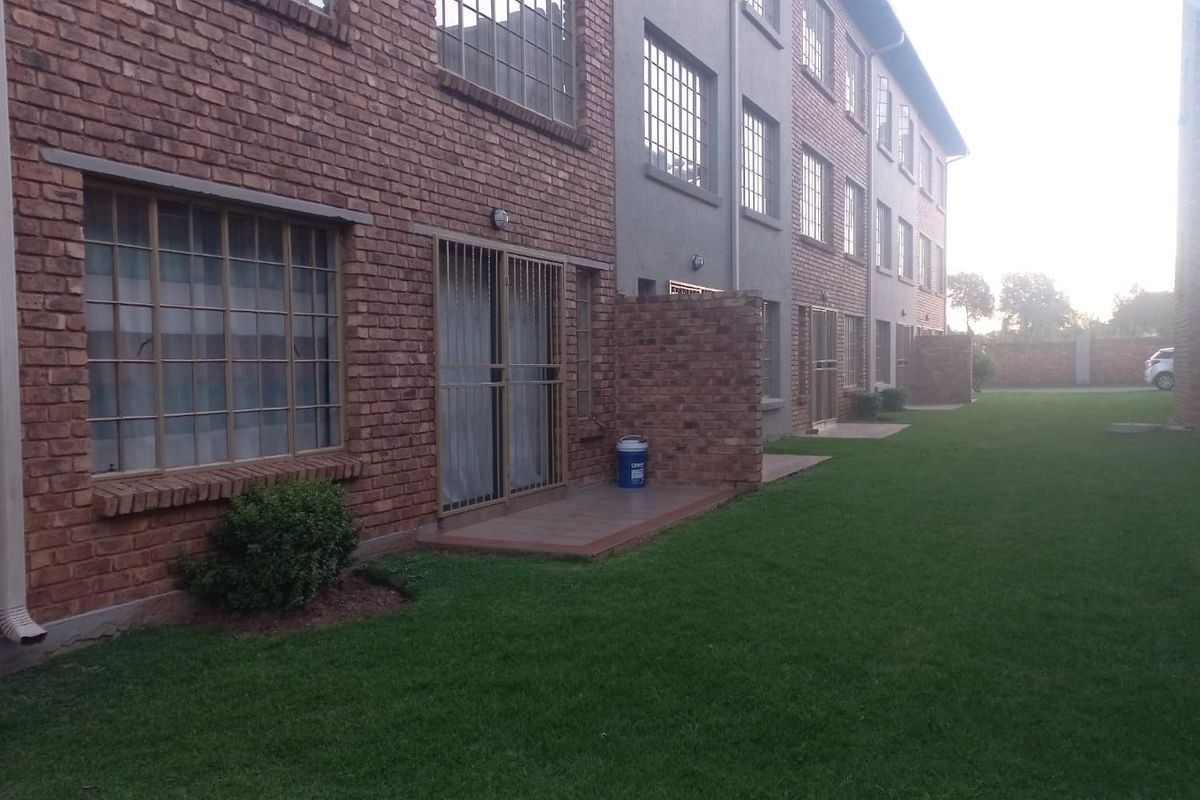 Exterior view of a multi-story apartment complex featuring face-brick facades, ground-level patio access, and a shared communal lawn area.