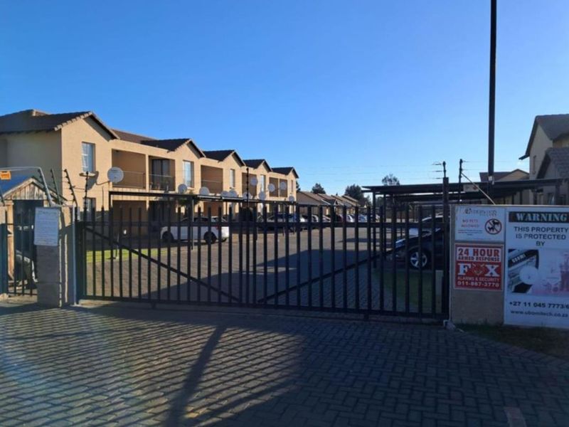 Front view of a townhouse complex featuring a secure gated entrance, paved driveway, and covered carport parking.