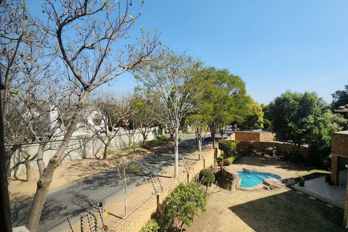 Elevated view overlooking the property grounds, featuring a small swimming pool, landscaped garden, and perimeter security fencing.