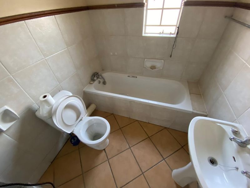 A dated bathroom featuring a built-in bathtub, pedestal basin, and toilet, finished with ceramic wall and floor tiles.