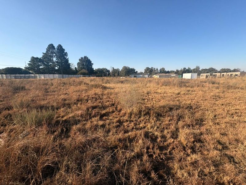 A wide-angle view of a vacant residential plot featuring dry grass and perimeter fencing, offering a blank canvas for future development.