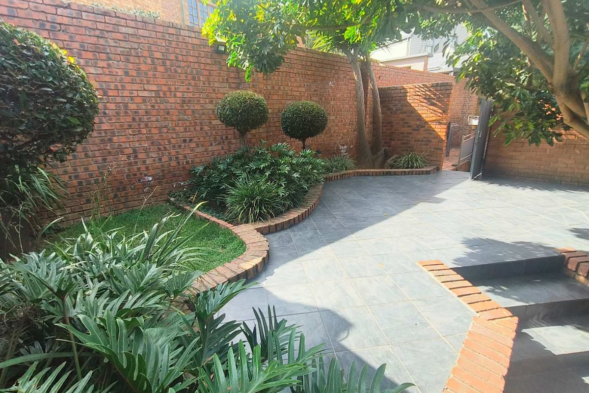 A well-maintained private rear garden featuring a paved patio area, brick boundary walls, and established landscaping.