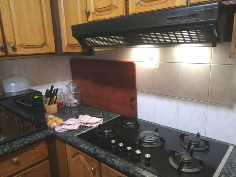 A functional kitchen area featuring wooden cabinetry, a black gas hob, an integrated extractor fan, and a granite countertop with tiled backsplash.