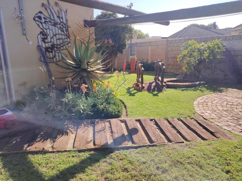 A private rear garden featuring a lawn, brick-paved circular area, timber sleeper pathway, and concrete boundary walling.
