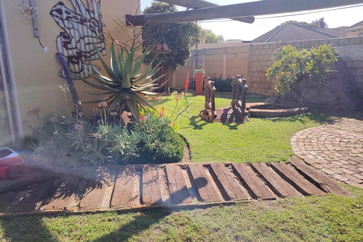 A private rear garden featuring a lawn, brick-paved circular area, timber sleeper pathway, and concrete boundary walling.