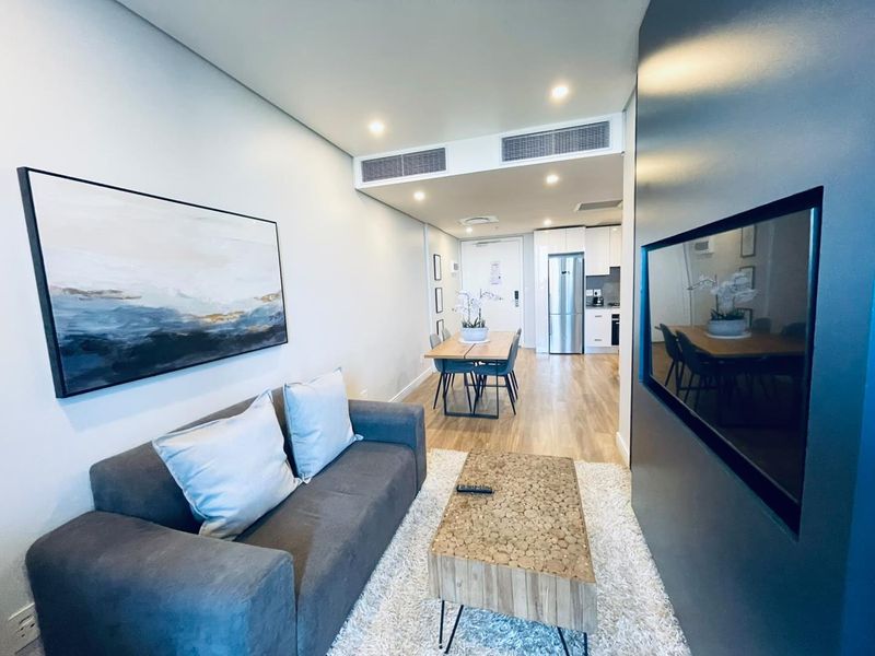 Modern open-plan living and dining area featuring sleek cabinetry, integrated appliances, recessed lighting, and ducted air conditioning in a contemporary apartment setting.