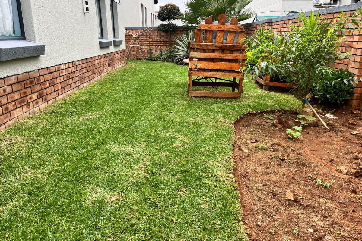A private rear garden area featuring a manicured lawn, perimeter brick boundary walls, and established garden beds.