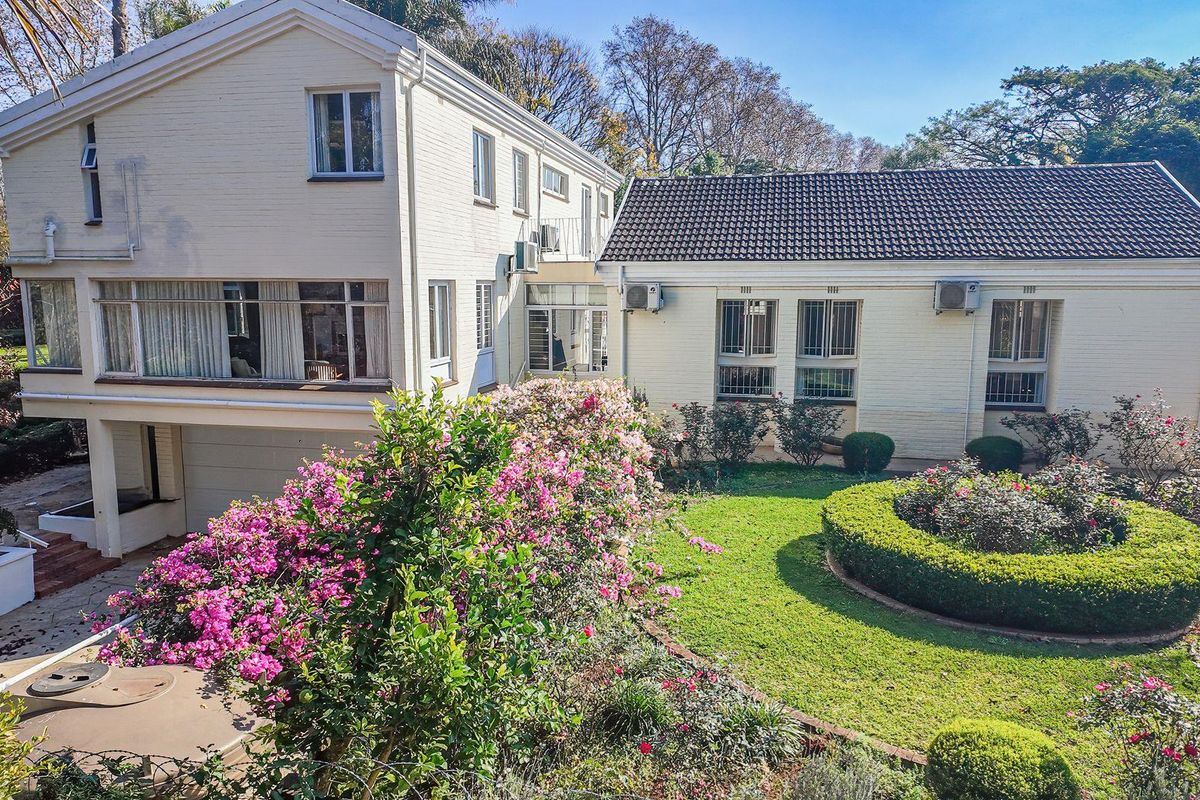 A view of the rear exterior of the two-story house, featuring a landscaped garden, manicured hedges, and established trees.