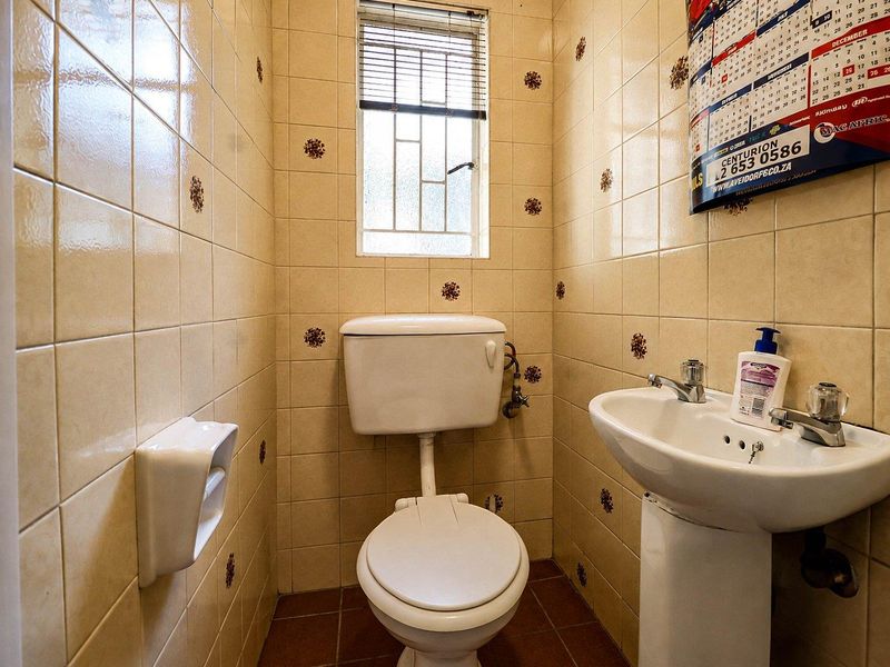 A compact guest bathroom featuring a pedestal basin, toilet, and dated ceramic wall tiles with decorative accents.