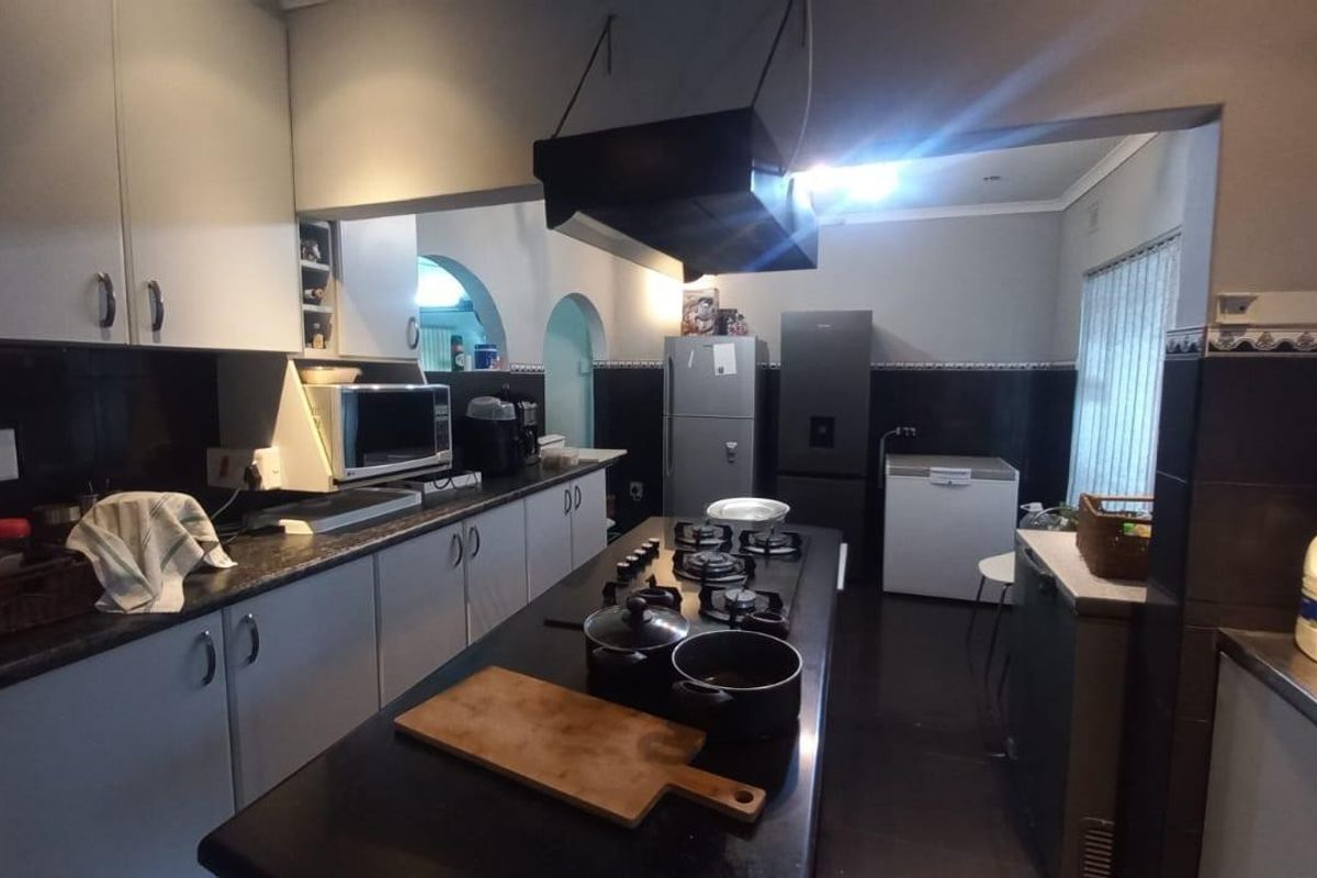 A functional kitchen featuring built-in cabinetry, dark countertops, a central gas hob with an overhead extractor fan, and tiled wall finishes.