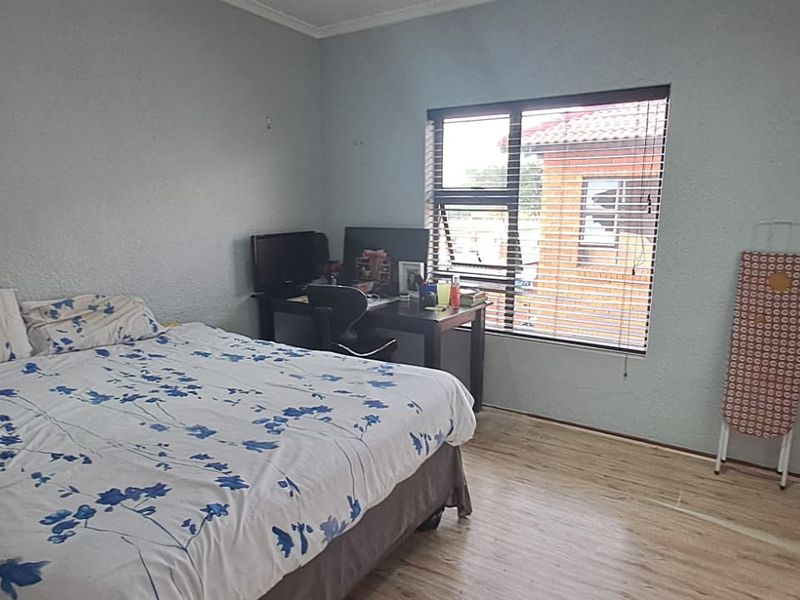 A bedroom featuring laminate flooring, built-in cupboards, and an aluminium window with venetian blinds.