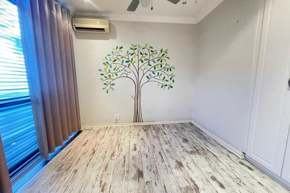 A bright, empty bedroom featuring light-toned laminate flooring, a ceiling fan, and a wall-mounted air conditioning unit.