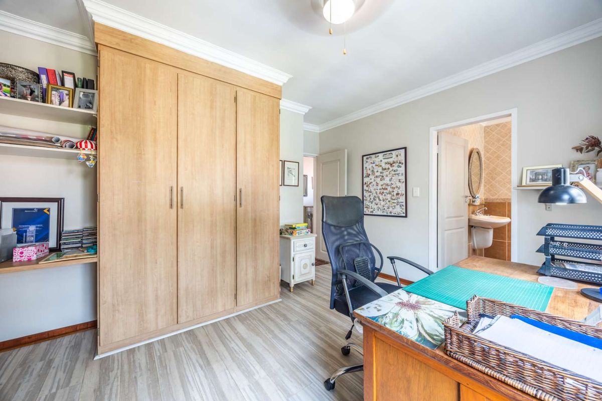 A well-maintained bedroom featuring light wood-look laminate flooring, extensive built-in cabinetry, crown molding, and direct access to an en-suite bathroom.