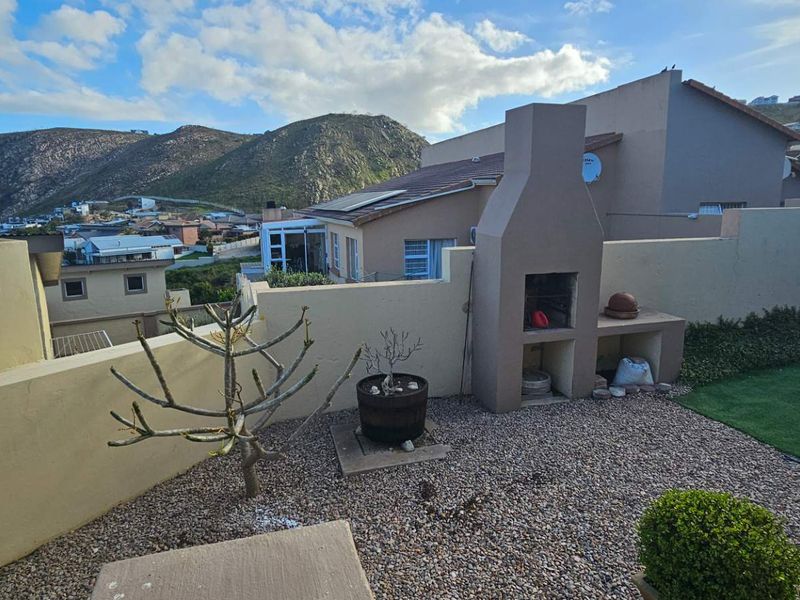 Rear garden area featuring a built-in braai, gravel landscaping, and artificial lawn, set against a scenic mountain backdrop.