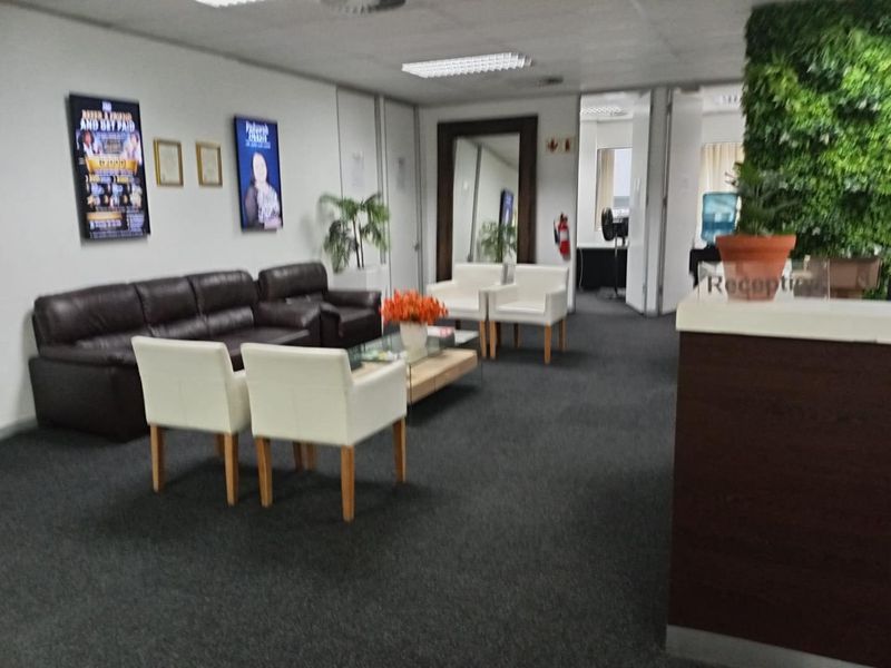 A professional office reception area featuring a dedicated reception desk, carpeted flooring, and recessed lighting, providing a functional waiting space for clients.