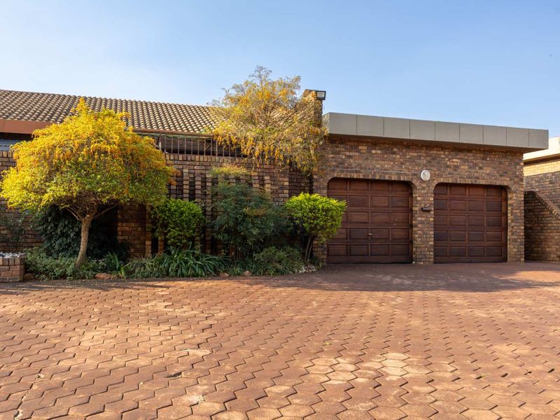 Front view of a townhouse featuring a double garage with wooden doors, a brick facade, and a paved driveway.
