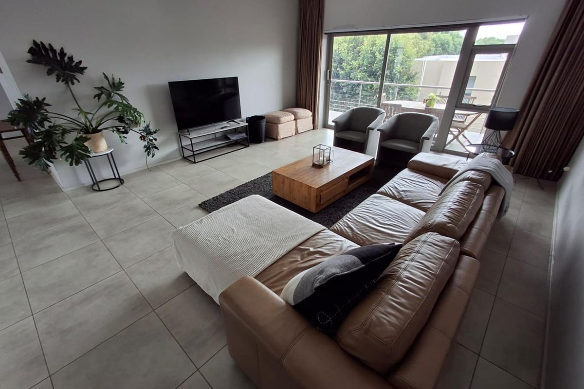 Spacious living room featuring large format floor tiles and a wide sliding glass door providing access to an outdoor balcony area.