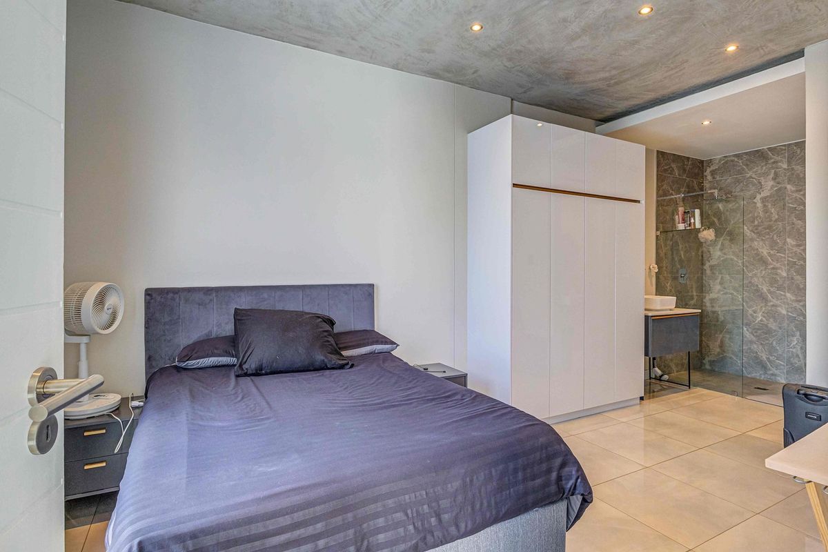 Modern bedroom featuring an exposed concrete ceiling, built-in wardrobe, and an open-plan en-suite bathroom with a glass shower enclosure and contemporary vanity.