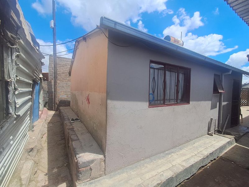 Rear exterior view of the property featuring a plastered wall, security bars on the window, and a roof-mounted solar water heater.