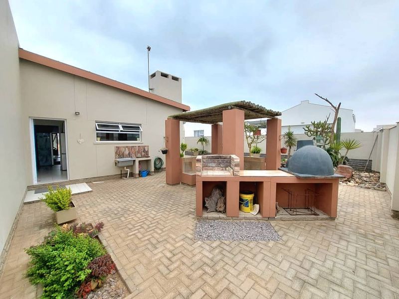 Outdoor entertainment area featuring a built-in brick braai, pizza oven, and covered prep station set within a paved courtyard.