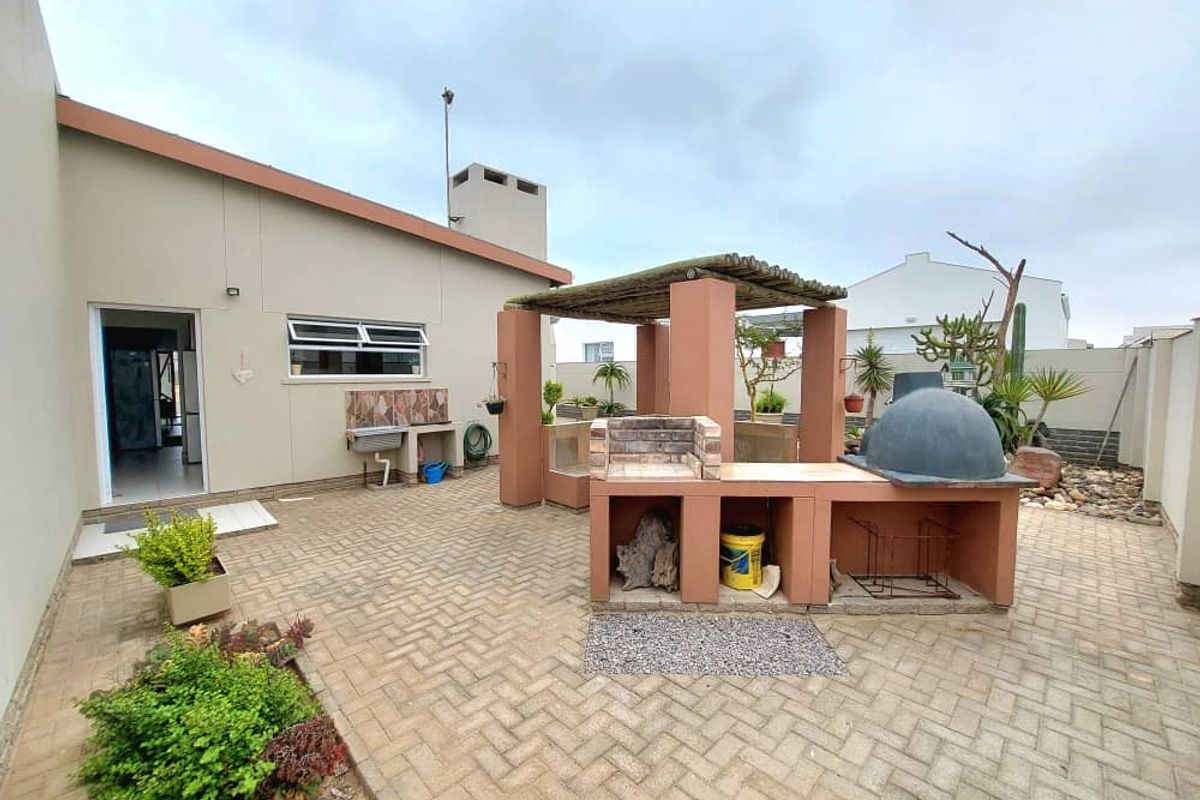 Outdoor entertainment area featuring a built-in brick braai, pizza oven, and covered prep station set within a paved courtyard.