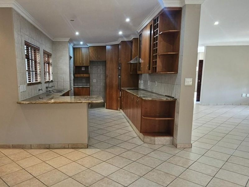 Spacious kitchen featuring wooden cabinetry, granite countertops, built-in oven, and tiled flooring, offering a functional layout with an open-plan flow to the living area.
