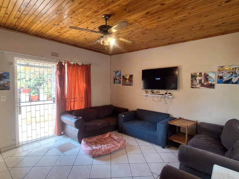 Living room featuring a timber tongue and groove ceiling, ceiling fan, tiled flooring, and direct access to an outdoor area via a security gate.