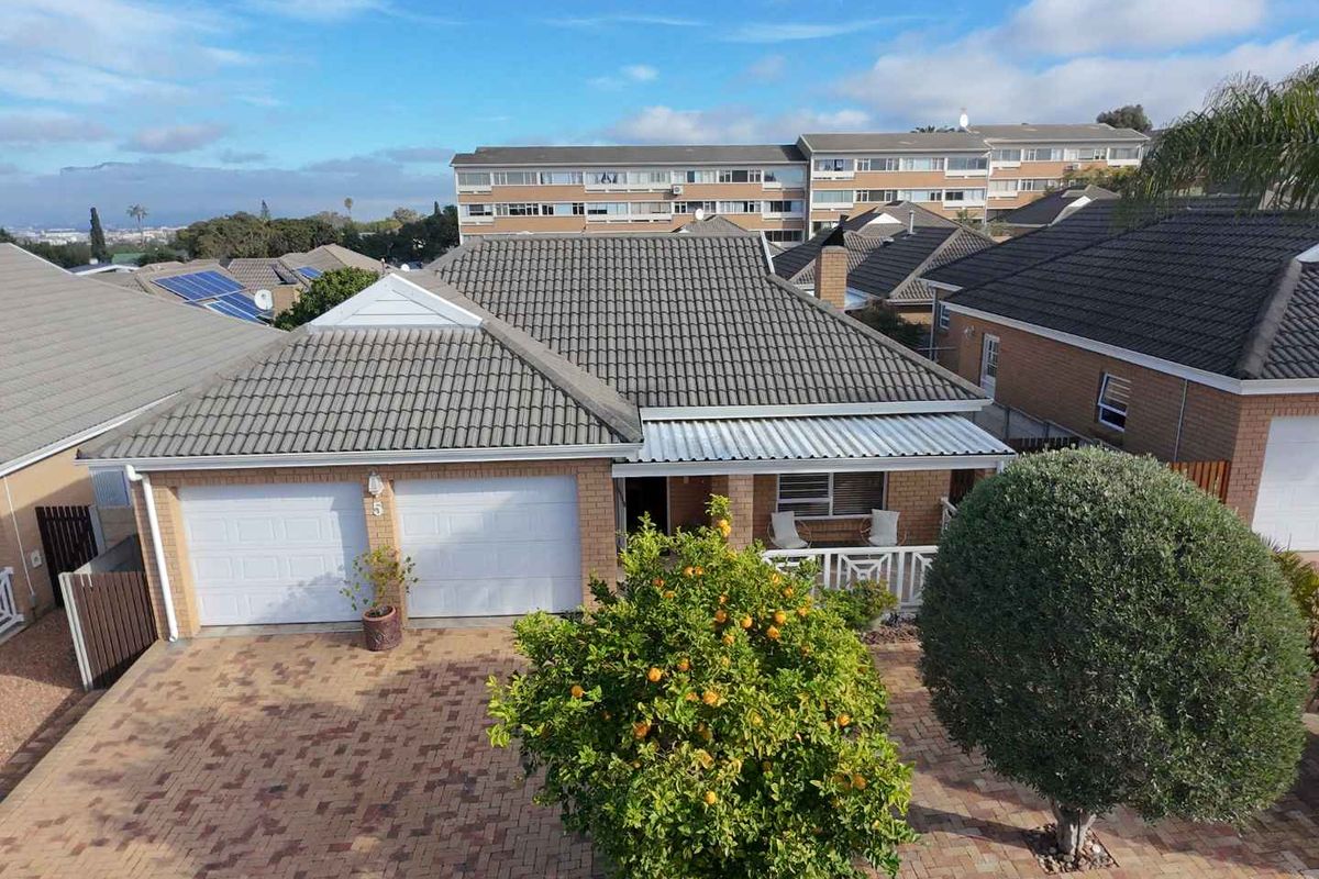 Aerial view of a townhouse featuring a double garage, paved driveway, tiled roof, and a covered front entrance area.
