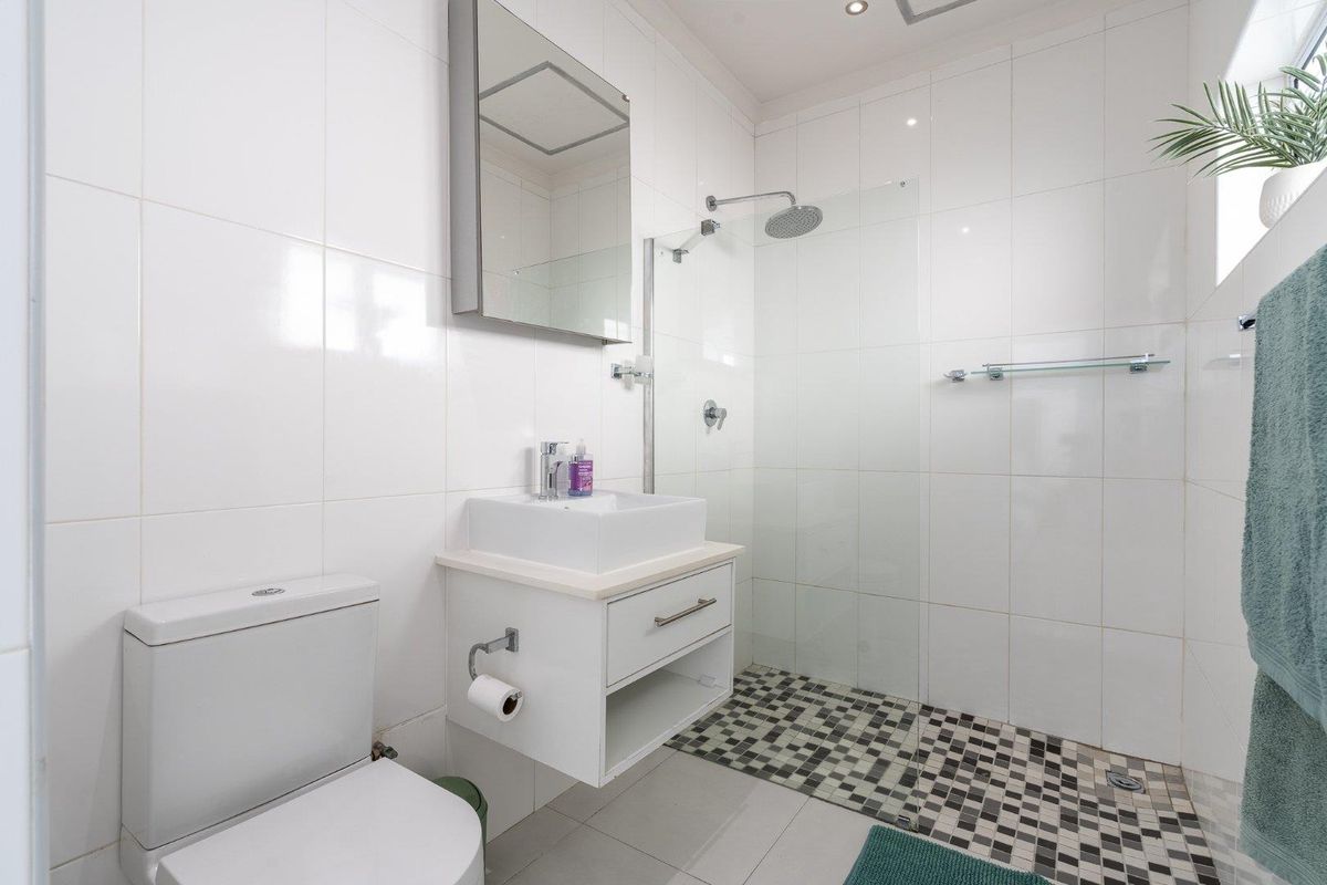 A modern bathroom featuring a walk-in shower with a rain shower head, mosaic floor tiling, a wall-mounted vanity, and a vessel sink.