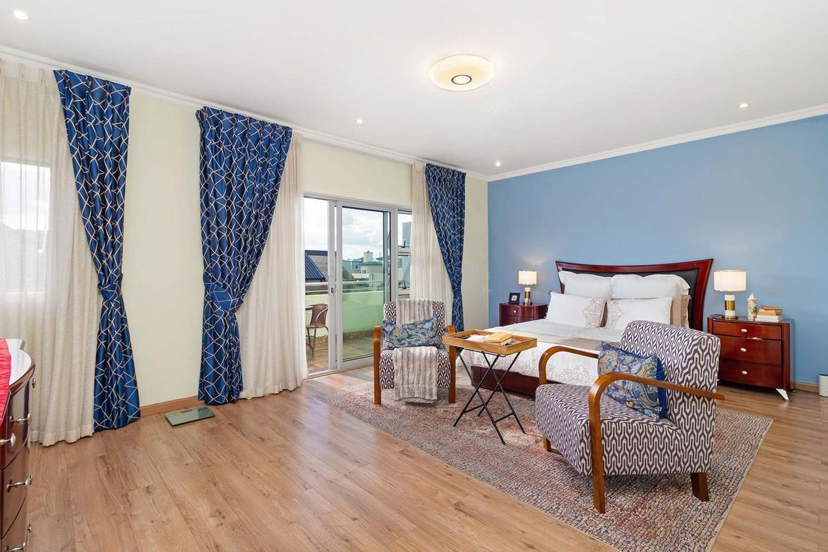 Spacious bedroom featuring wood-look flooring, a blue accent wall, and sliding glass doors leading to a private balcony.