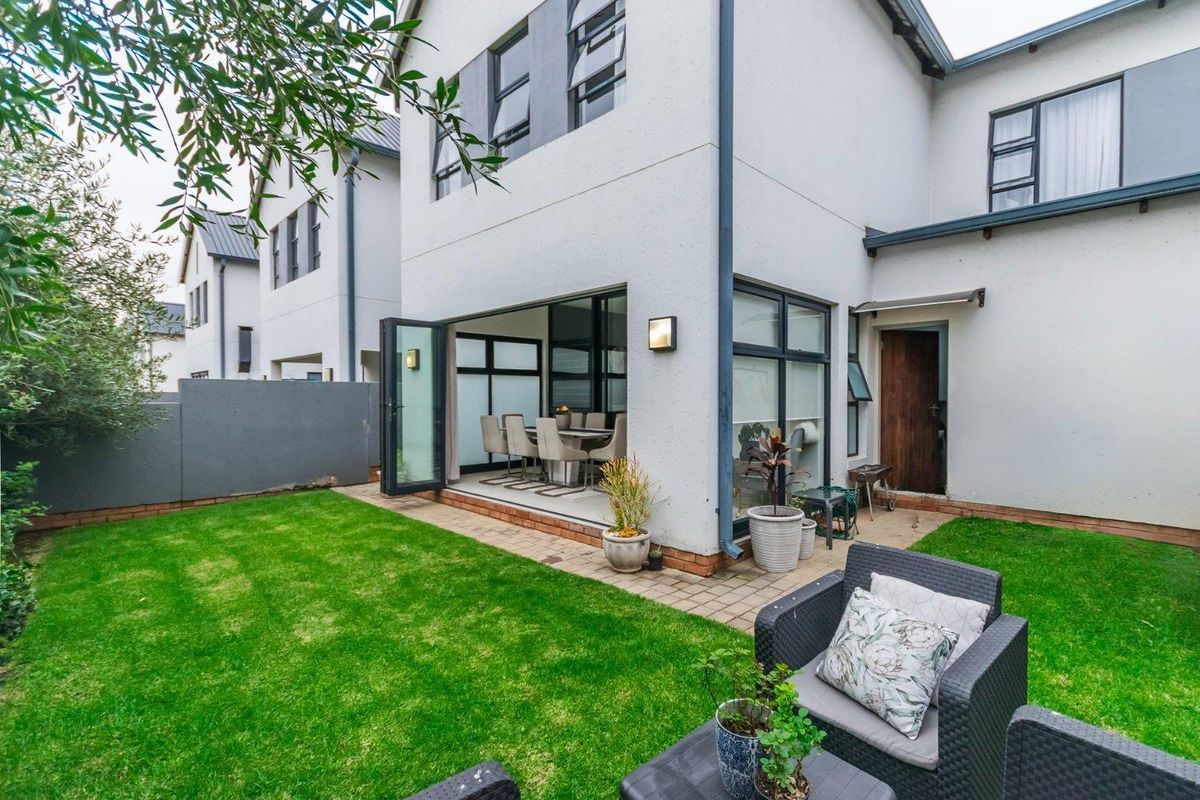 Rear view of a modern townhouse featuring a landscaped garden, paved patio area, and large bi-fold doors leading into the interior living space.