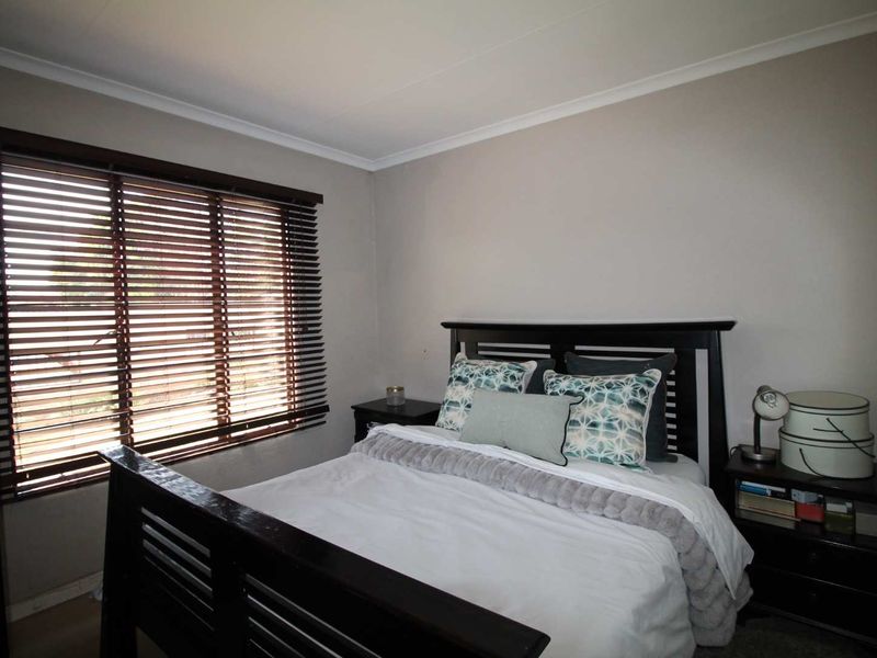 A well-maintained bedroom featuring neutral wall tones, cove cornicing, and fitted wooden venetian blinds.