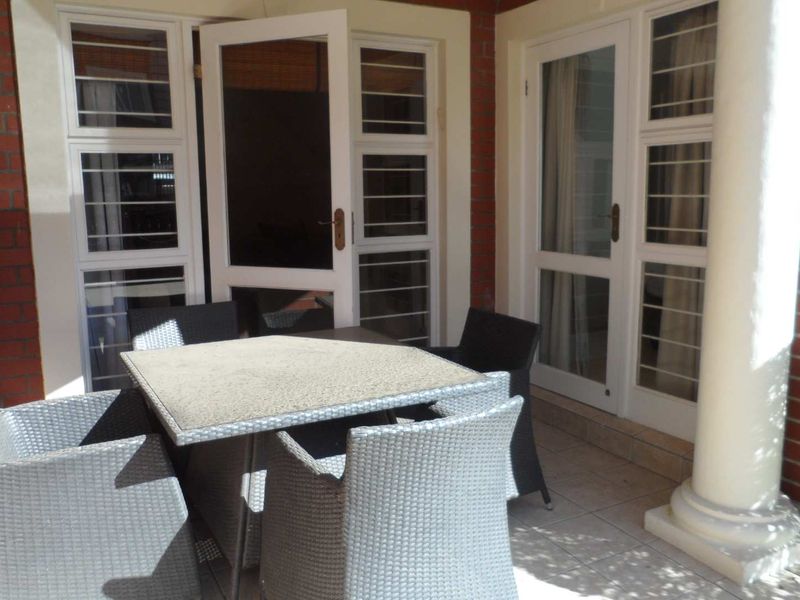 A covered patio area featuring tiled flooring, brick wall accents, and white-framed glass doors providing access to the interior.