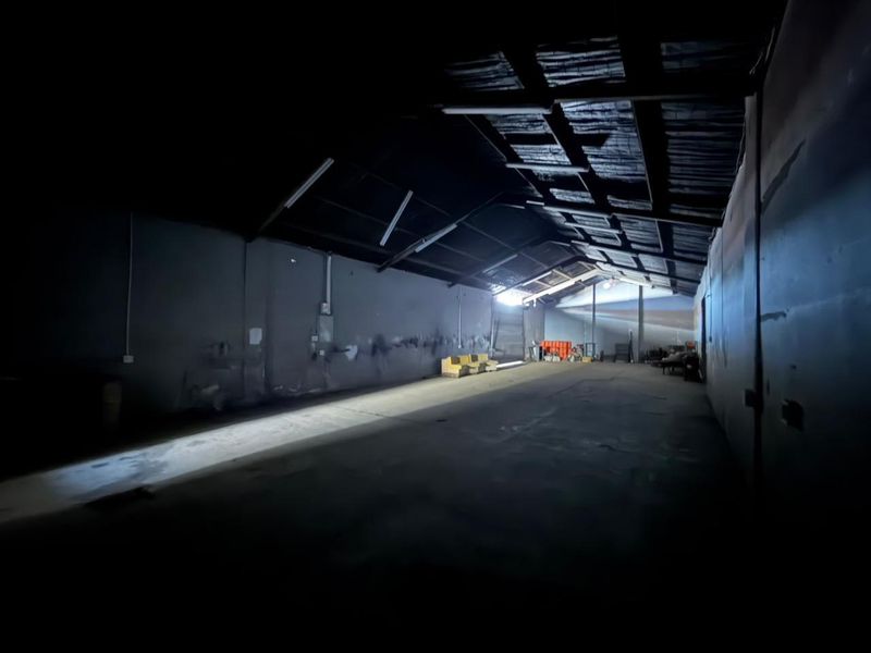 Spacious industrial utility area featuring exposed timber roof trusses, concrete flooring, and a large roller door, suitable for storage or workshop use.