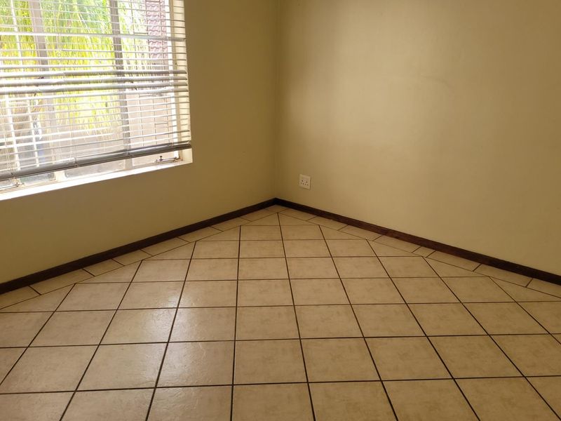 A vacant bedroom featuring neutral tiled flooring, skirting boards, and a window fitted with venetian blinds.
