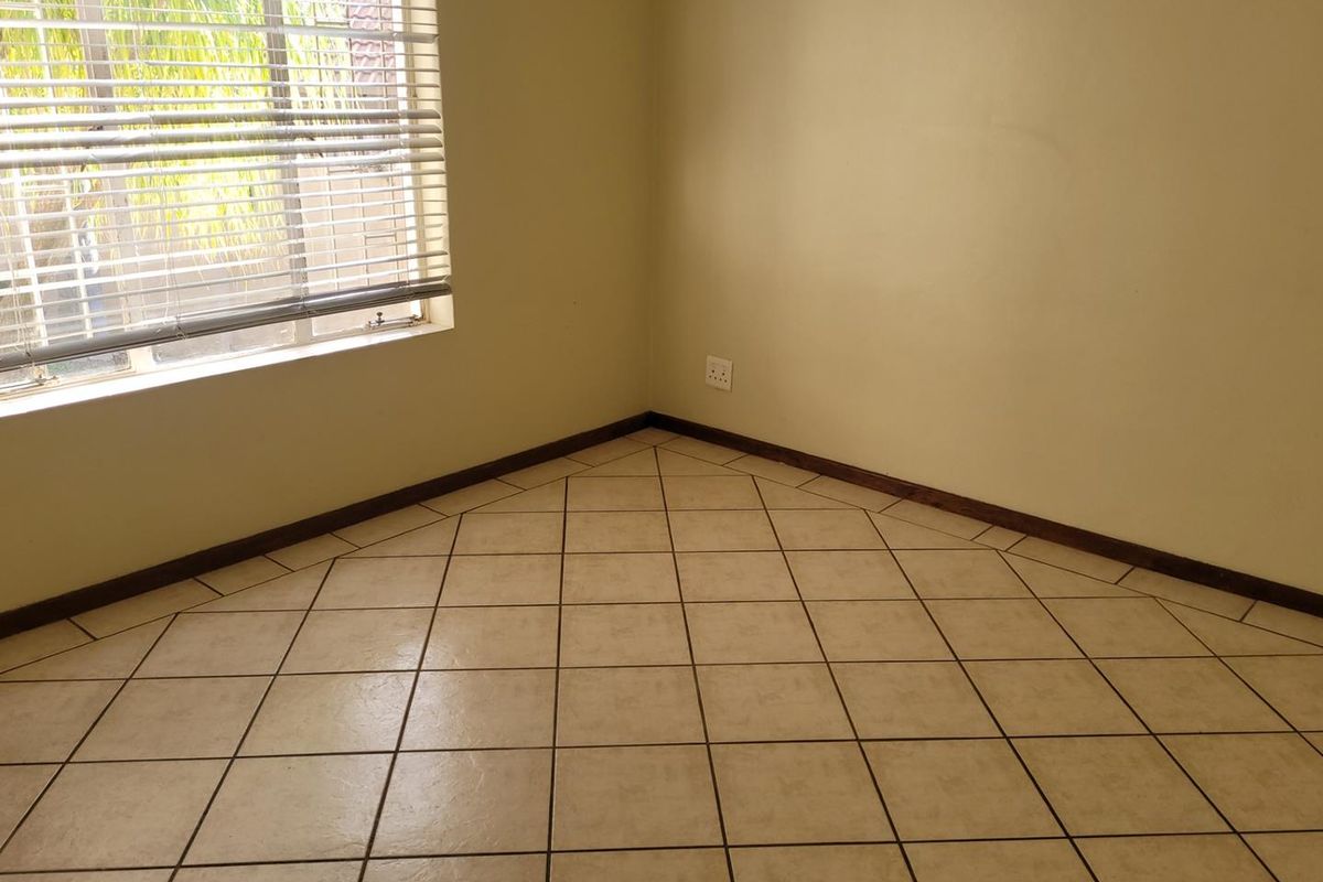A vacant bedroom featuring neutral tiled flooring, skirting boards, and a window fitted with venetian blinds.
