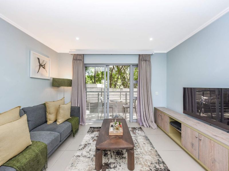 A bright and well-maintained living room featuring tiled floors, recessed lighting, and a sliding glass door providing access to an outdoor balcony area.