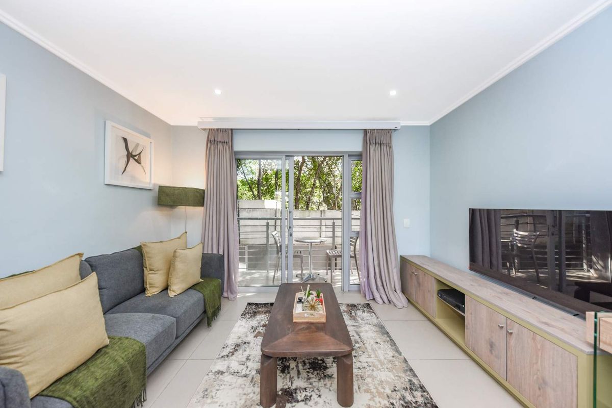 A bright and well-maintained living room featuring tiled floors, recessed lighting, and a sliding glass door providing access to an outdoor balcony area.