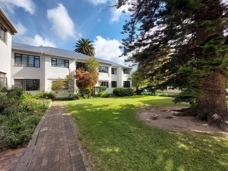 A view of the apartment building exterior featuring a well-maintained lawn, mature trees, and a brick paved pathway leading to the residential units.