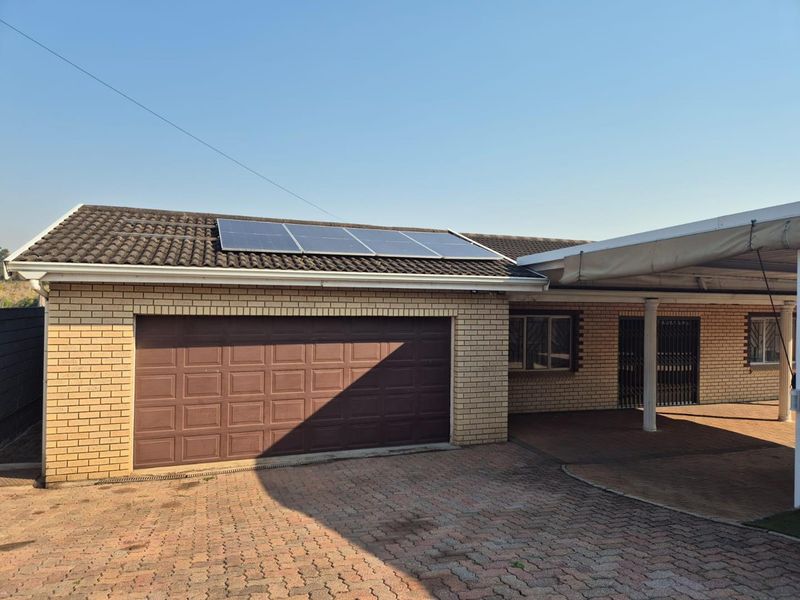 Front exterior view of a brick house featuring a garage, carport, and roof-mounted solar panels with a paved driveway.