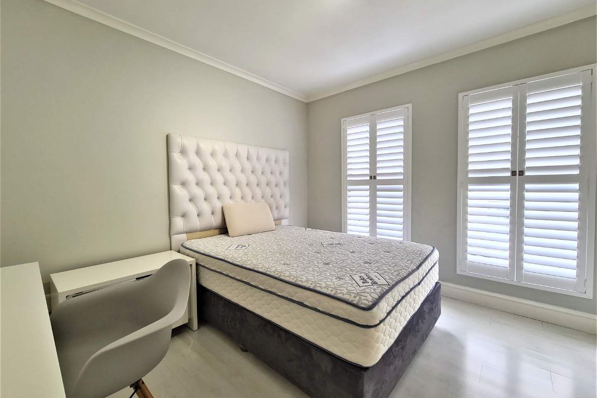 A bright bedroom featuring light-toned flooring, neutral walls, and white plantation shutters on the windows, providing a clean and modern aesthetic.