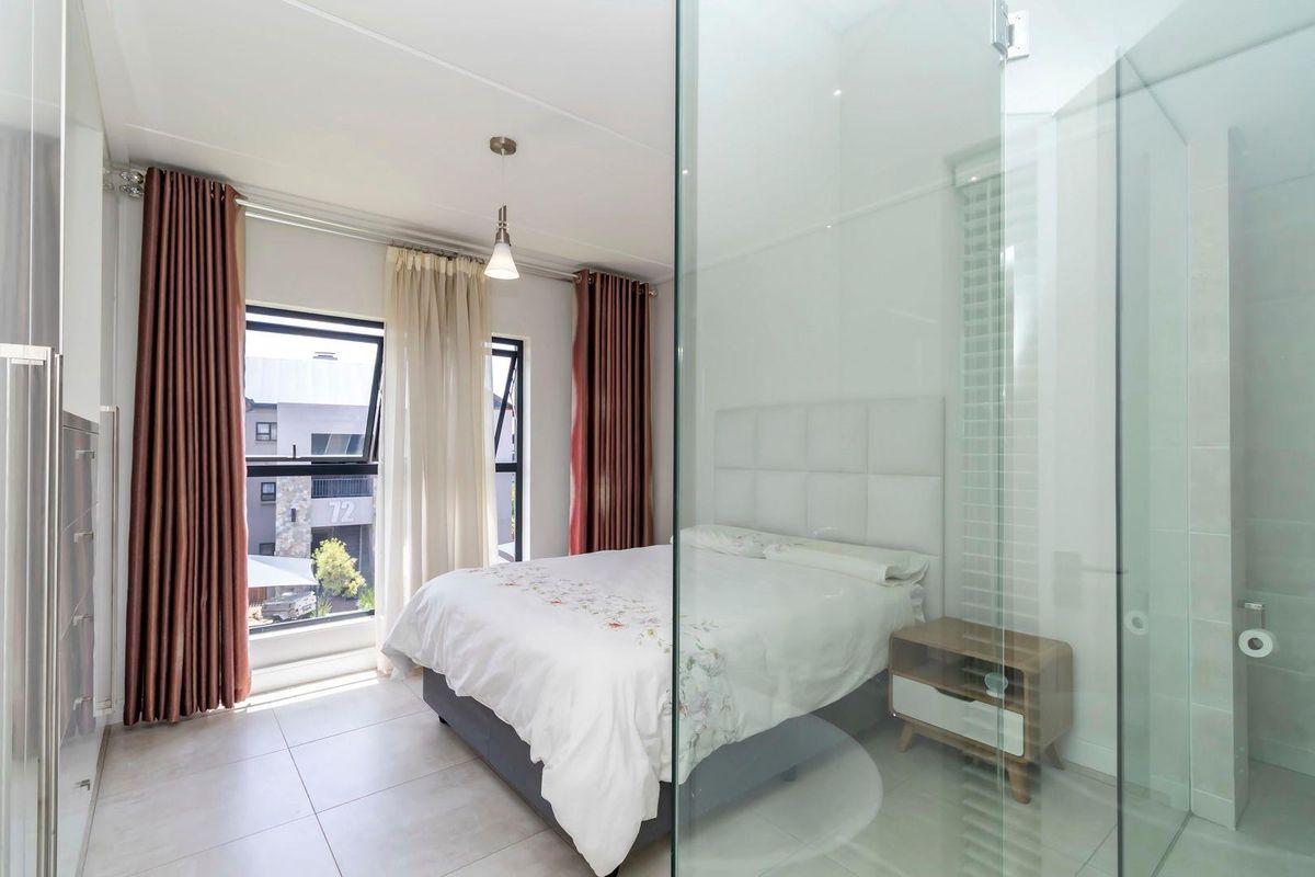 Modern bedroom featuring tiled flooring, large windows with curtains, and an integrated glass-enclosed en-suite bathroom.